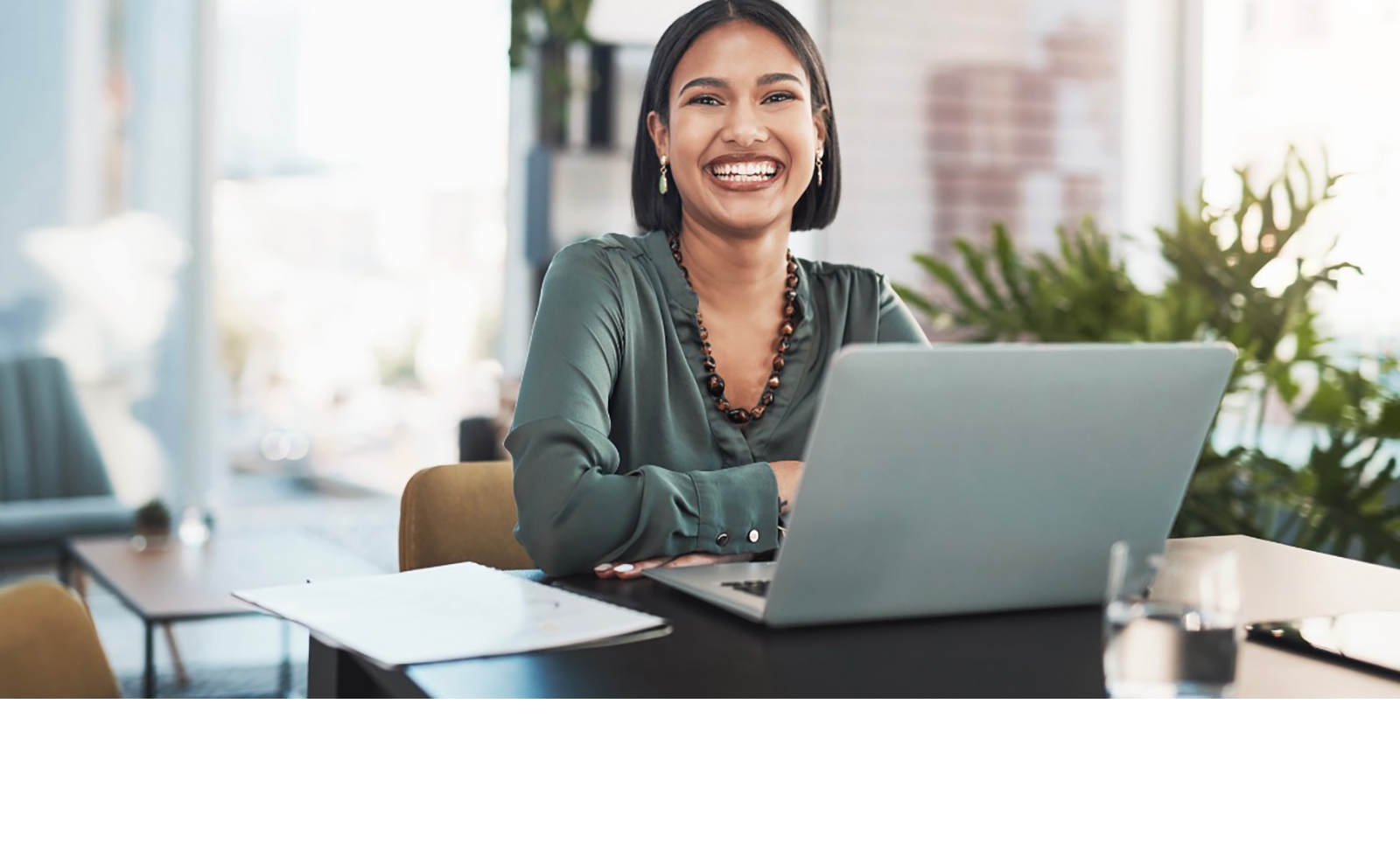 Young Asian woman smiling at camera, seated at table with laptop.