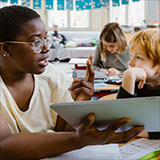 Teacher assisting student with using a tablet in class.