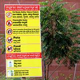 Yellow sign listing prohibited and allowed items with a brick wall in the background and a small tree
