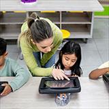 Teacher assisting a student with using her tablet in class.