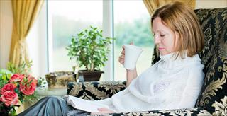 woman relaxing with book and warm drink at home