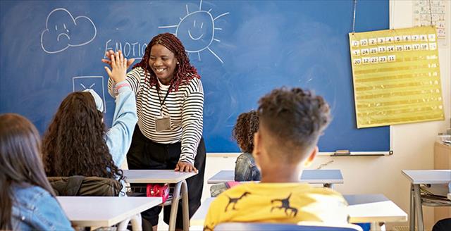 teacher and schoolgirl exchanging high-five in classroom