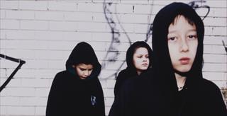 young men in dark hoodies standing by spraypainted wall
