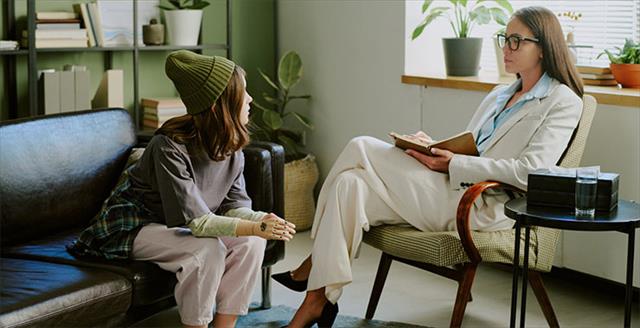 Therapist in white suit sitting opposite young patient on couch during session discussing problems
