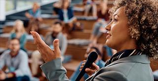 Female professor delivers presentation in front of audience.