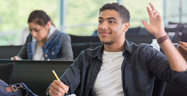 Young male college student raises his hand to ask a question in class.