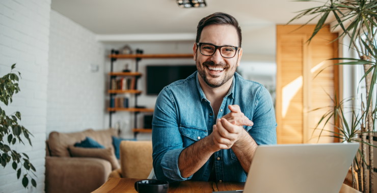Man clasping hands and smiling near his laptop