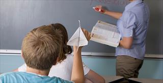 Young boy throwing a paper airplane in class.