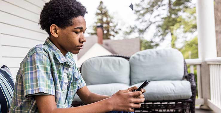 Adolescent sitting on a porch and looking at a smartphone.