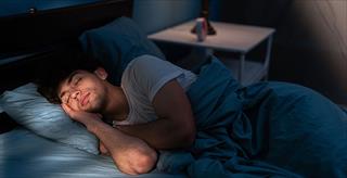 Peaceful young man sleeping in a comfortable bed alone at home
