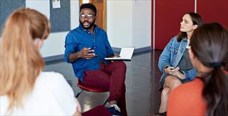Young college professor leads discussion among circle of students.