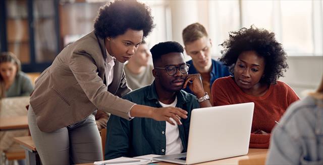 Two students and an educator gathered around a laptop talking