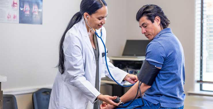 A clinician uses a stethoscope and blood pressure cuff to examine a seated patient in a clinical setting.
