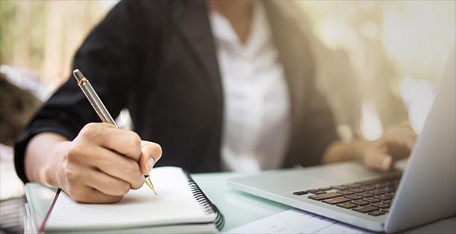 Young female student studying making note on notebook and using laptop