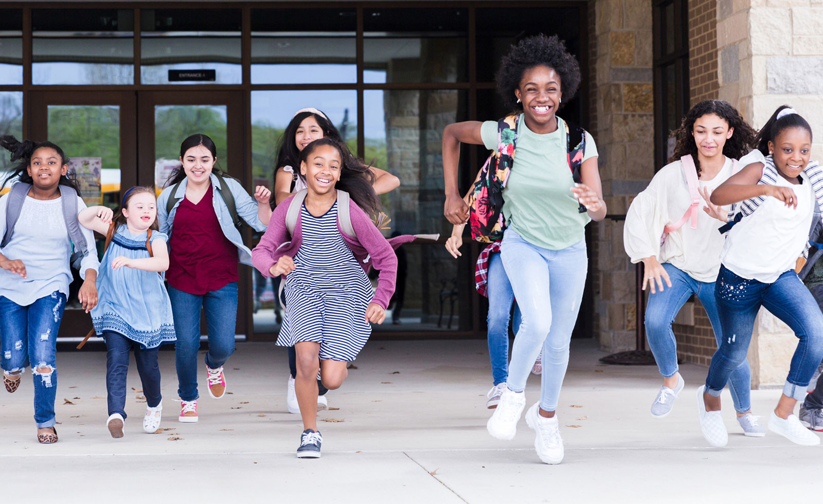 Diverse group of children bursting through the school doors to leave for the day.